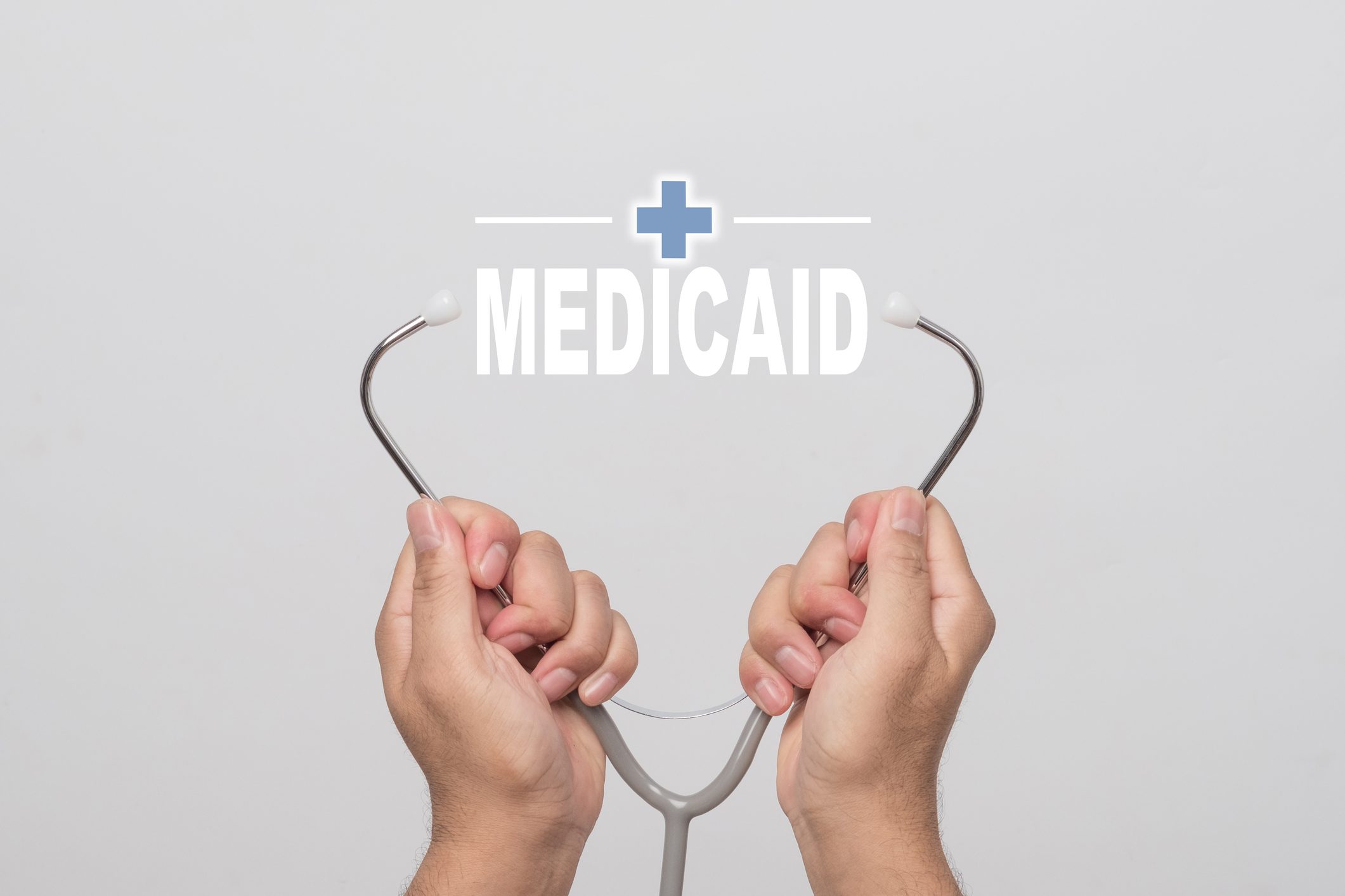 Hands holding a stethoscope with the word Medicaid between the earpieces.