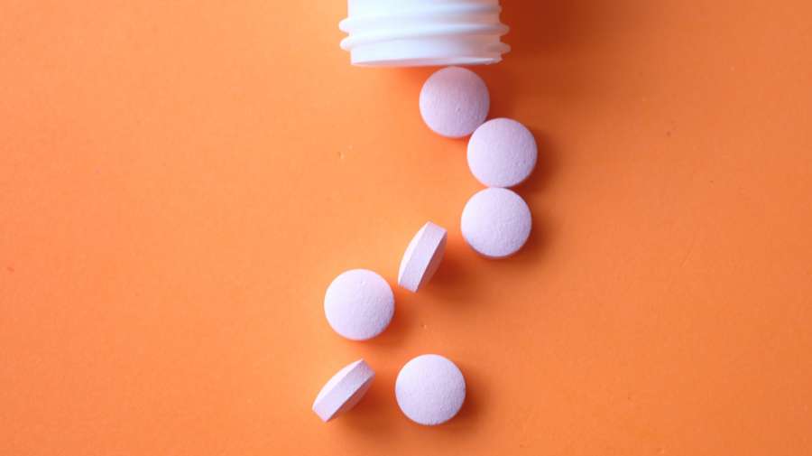 White Pills Spilling from Bottle on Orange Backdrop